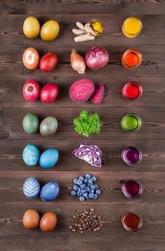 an array of different colored eggs on a wooden table next to some fruit and vegetables