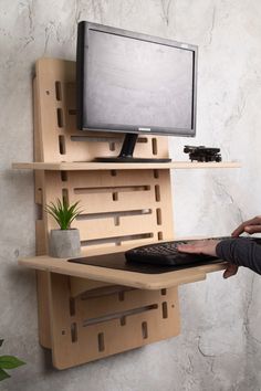 a person holding a keyboard and mouse in front of a computer monitor on a wooden shelf