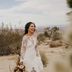 a woman in a white dress is walking through the desert with her bouquet and smiling