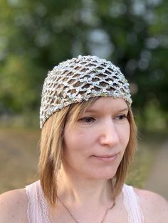 a woman wearing a crocheted headband in front of trees