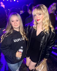 two women standing next to each other in front of a purple light at a party