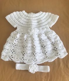 a white crocheted dress and headband on a brown surface with a tan background