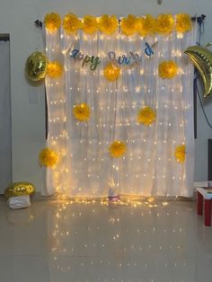 a birthday party with balloons and streamers on the wall, yellow flowers in front of a white curtain