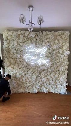 a man kneeling down in front of a white flower wall with the words happily wed to each other