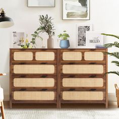 a wooden dresser sitting next to a wall with pictures above it and plants on top