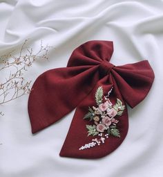 a red bow with flowers on it laying on a white sheet next to dried plants