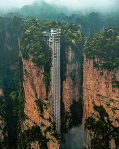 an aerial view of a tall building in the middle of some mountains with trees on top