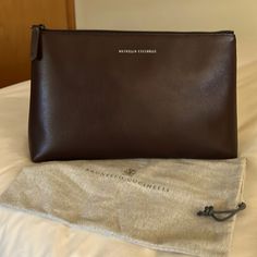 This Georgous Authentic Brunello Cucinelli Calf-Skin Super Soft Leather Clutch Bag In A Deep Rich Dark Brown Almost Has A Hint Of Maroon In Certain Lighting (Please See Pictures). It Has Gun Metal Hardware And Signature Lettering At The Front And A Leather Stitch Tag Inside With A Nylon Lining. This Beautiful Bag Is New Without Tags. It Has Never Been Carried. I Do Have The Dust Bag Which Is Also Pictured Msrp $1400 L 13” H 8” W 3.5” Elegant Pouch-style Business Clutch, Elegant Business Clutch In Pouch Shape, Elegant Business Clutch Shaped As A Pouch, Brown Luxury Business Pouch, Luxury Brown Business Pouch, Elegant Leather Travel Pouch, Modern Formal Pouch With Dust Bag, Luxury Formal Pouch With Dust Bag, Luxury Formal Pouch With Dust Bag Included