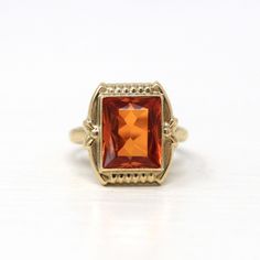 Beautiful vintage circa 1940s Retro era created orange sapphire ring! This pretty ring features a rectangular faceted 3.95 carat created orange sapphire stone, that is securely bezel set. The piece has a stylish setting with sweet floral shoulders. A gorgeous piece of fine retro jewelry, featuring a stunning bright orange stone! ERA - Circa 1940s - Retro METAL / MATERIAL - 10k yellow gold, created orange sapphire (approx. 3.95 CT)  MARKINGS / HISTORY - Inside of the band is marked 10k CONDITION - Good vintage condition. Yellow gold metal has been professionally polished & cleaned. Created orange sapphire is securely set. Some tarnish wear remains. Amazing vintage created orange sapphire ring!  SIZE / MEASUREMENTS - Size: 3, Ring Head Height: 14 mm, Back of Shank: 1.6 mm, Created Orange Sap Classic 14k Gold Orange Jewelry, Classic Orange 14k Gold Jewelry, Classic Orange Topaz Ring For Anniversary, Classic Orange 14k Gold Ring, Classic Orange Rings For Anniversary, Classic Orange Ring Jewelry, Orange Heirloom Ring In 14k Gold, Heirloom Style 14k Gold Orange Ring, Heirloom 14k Gold Orange Ring