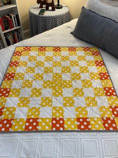 a bed with a yellow and white quilt on top of it next to a book shelf