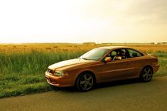 a brown car parked on the side of a road in front of some tall grass