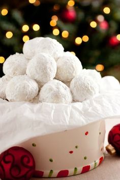 a white bowl filled with snowballs on top of a table next to a christmas tree