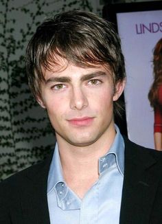 a man in a blue shirt and black blazer posing for the camera with a poster behind him