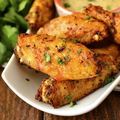 some chicken wings are on a white plate with dipping sauce and parsley in the background