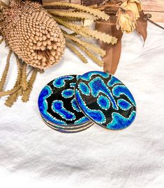 two blue and black plates sitting on top of a white table cloth next to dried plants