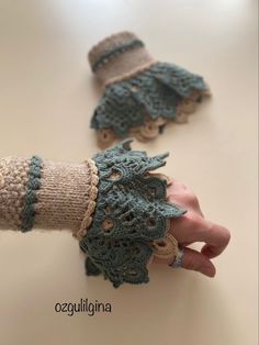 two crocheted gloves are shown with one being held by the other, on a table