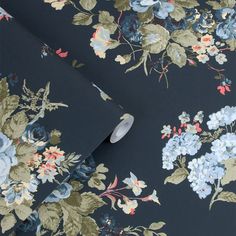 a black floral wallpaper with blue and pink flowers on it's side, next to a roll of toilet paper