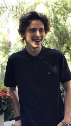 a young man standing in front of a potted plant and smiling at the camera