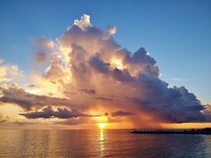 the sun is setting over the ocean with clouds in the sky and water below it