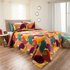 a bed with colorful bedspread and pillows on top of it in a room