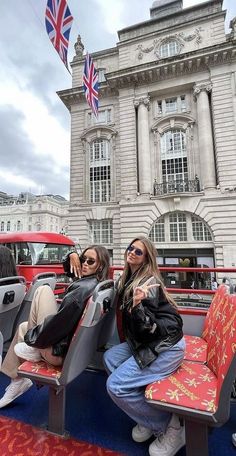 two women sitting on seats in front of a building with a british flag flying above them