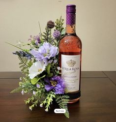 a bottle of wine sitting on top of a wooden table next to flowers and greenery