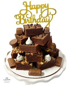 a white plate topped with brownies and marshmallows next to a happy birthday cake