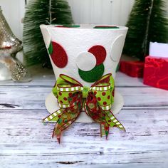 a white cup decorated with red, green and white polka dot bows on top of a wooden table