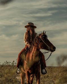 a man with long hair riding on the back of a brown horse in a field