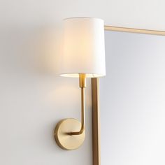 a wall mounted light with a white shade on it's side and a mirror in the background