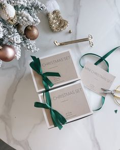 two boxes with green ribbon tied around them on a table next to ornaments and scissors