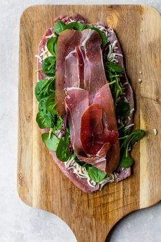 a wooden cutting board topped with sliced meat and veggies on top of it