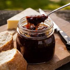 a spoon full of jam sitting next to bread on a cutting board