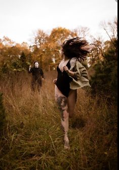 two people running through tall grass with trees in the background