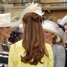 two women are talking to each other in front of a group of people wearing hats