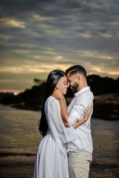 a man and woman standing next to each other in front of the ocean at sunset