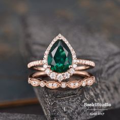 a close up of a ring with a pear shaped green stone and diamonds on it