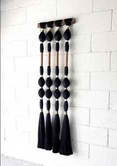 a black and white wall hanging with tassels on it's sides next to a brick wall