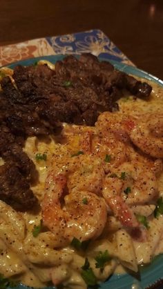 a blue plate topped with pasta covered in meat and shrimp next to veggies