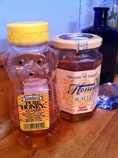 two jars of honey sitting on top of a wooden table