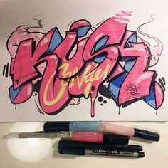 some pink and blue graffiti on top of a white board with black marker pens next to it