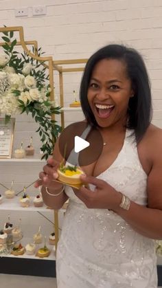 a woman in a white dress holding a plate with food on it and smiling at the camera