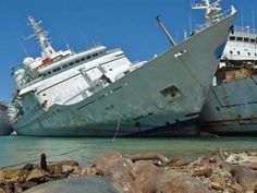 two large ships are docked in the water next to rocks and pebbles on the beach