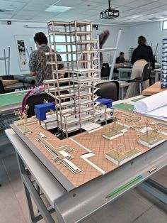 a model of a building being constructed on a table in a room with other people