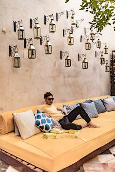 a man laying on top of a yellow couch next to a wall with hanging lights