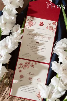 a red and white wedding card with flowers on it next to a bouquet of carnations