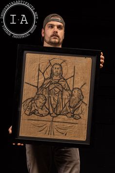 a man holding up a framed drawing of jesus