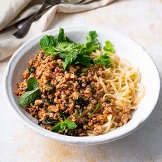 a white bowl filled with pasta and meat next to a fork on top of a table