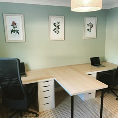 an office desk with two black chairs and a laptop on it in front of three framed pictures