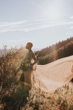 a woman standing on top of a lush green hillside holding a bouquet of white and yellow flowers